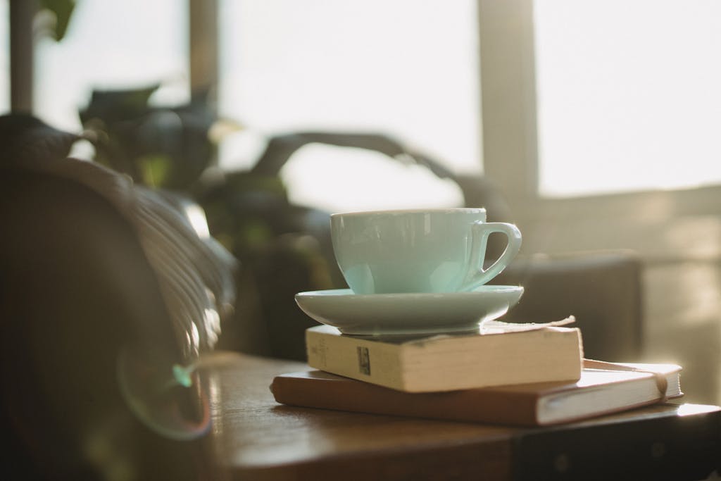 White ceramic cup of tea with plate and worn book with notebook placed on table