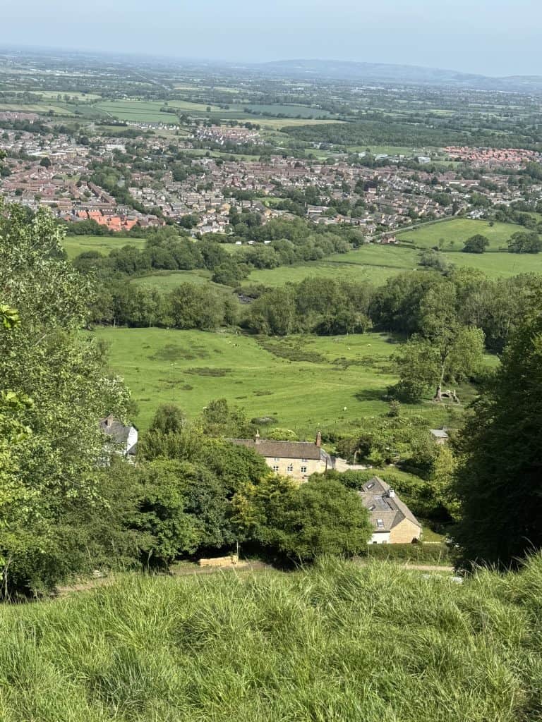 Panoramic view from Cooper's Hill looking across green fields, woodlands, and towns spread across the Severn Vale. The elevated viewpoint rewards walkers with one of the broadest vistas on the Cotswold Way.