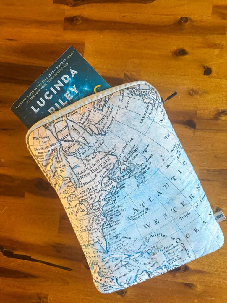 Photo of paperback book peeking out of quilted book cover with map design