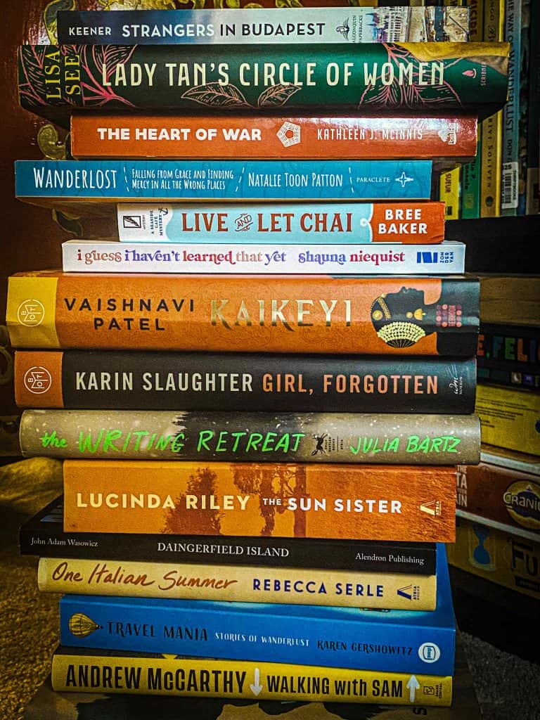 A tall stack of fiction and nonfiction books, including travel, thrillers, and memoirs, ideal for anyone looking to read more across a range of genres.